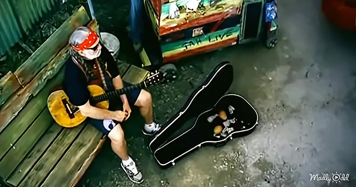 A person in a bandana plays guitar on a wooden bench, with an open guitar case nearby.