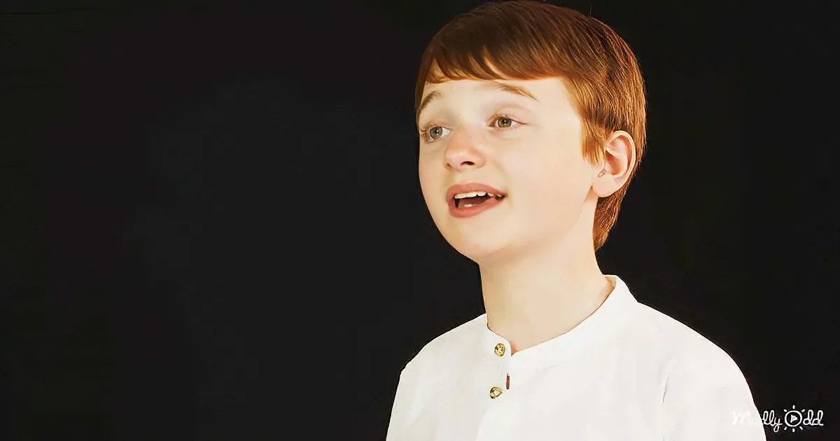 A young boy with short brown hair and a white shirt is looking up with his mouth slightly open.