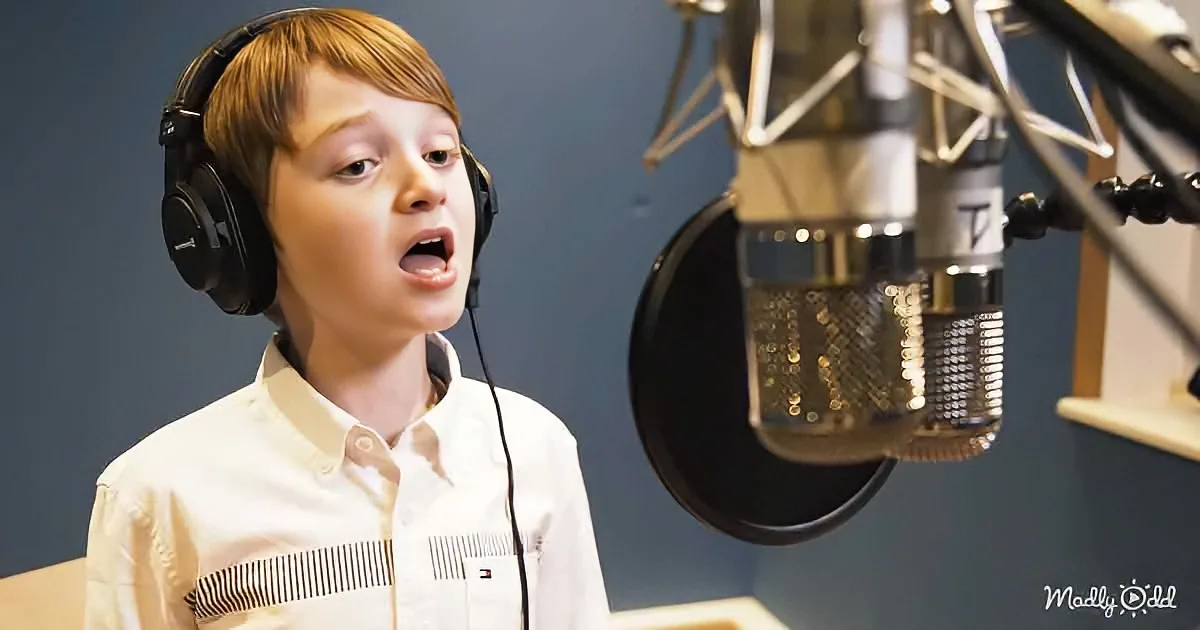 A young boy wearing headphones sings into a microphone in a recording studio.