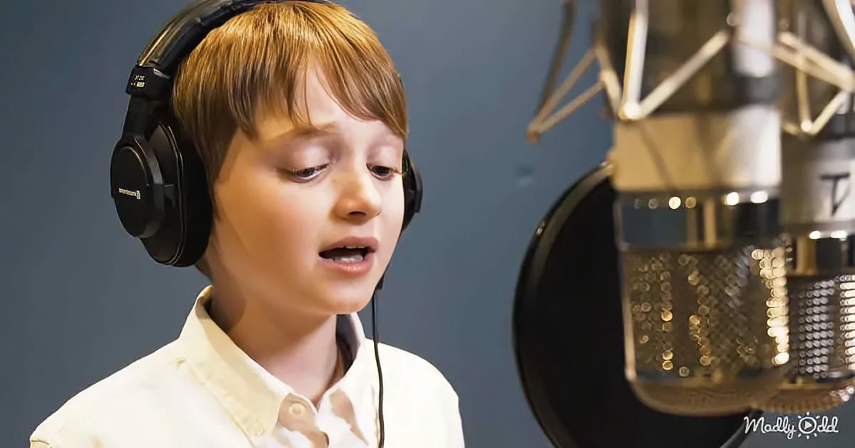A young boy wearing headphones sings into a microphone in a recording studio.