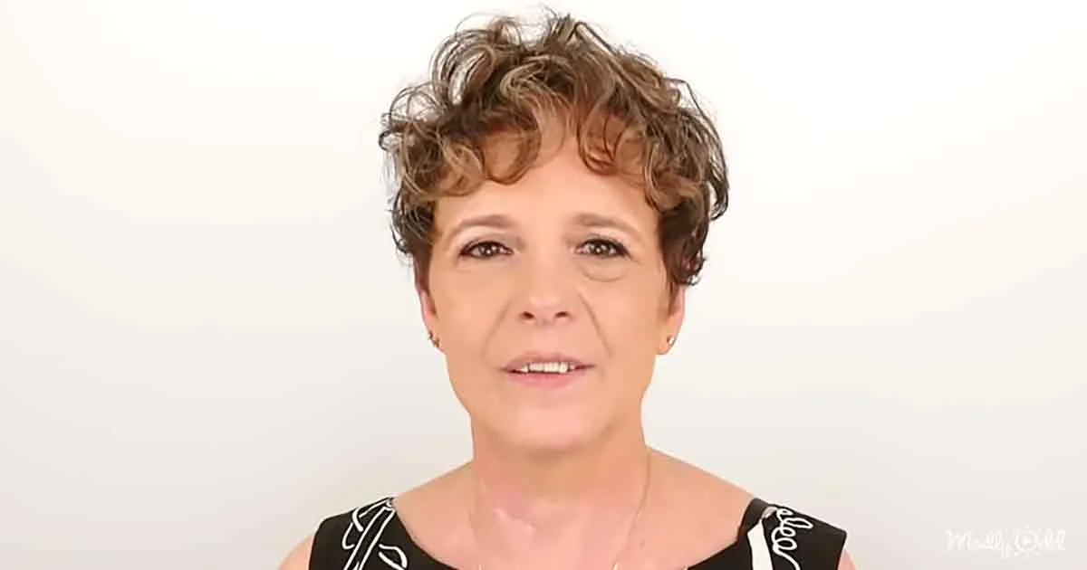 A woman with short, curly hair and a black and white top smiles against a plain white background.
