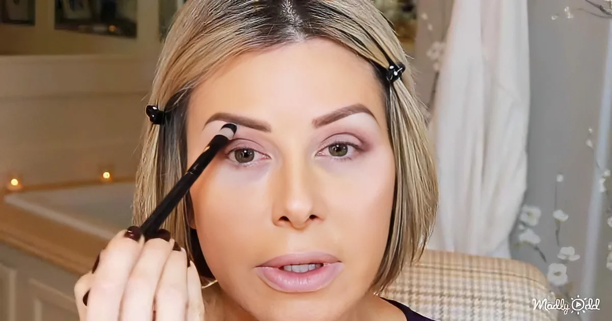 A woman with blonde hair and a black hair clip is applying makeup with a brush.