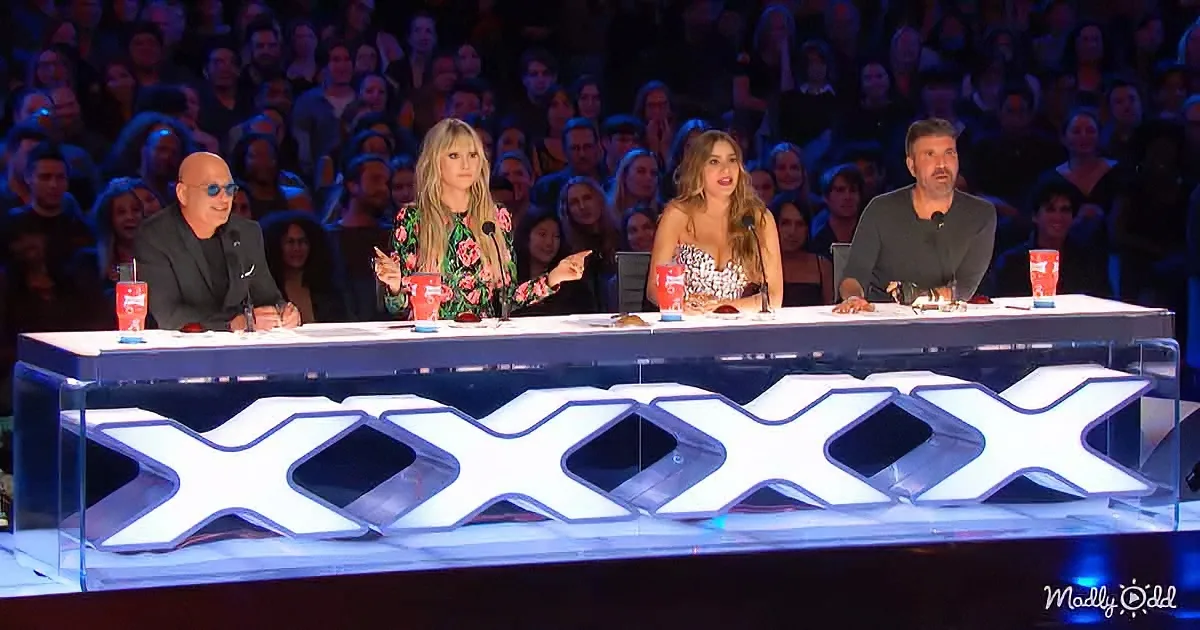 Judges on a panel with "XXXX" sign, audience in the background, colorful setting.