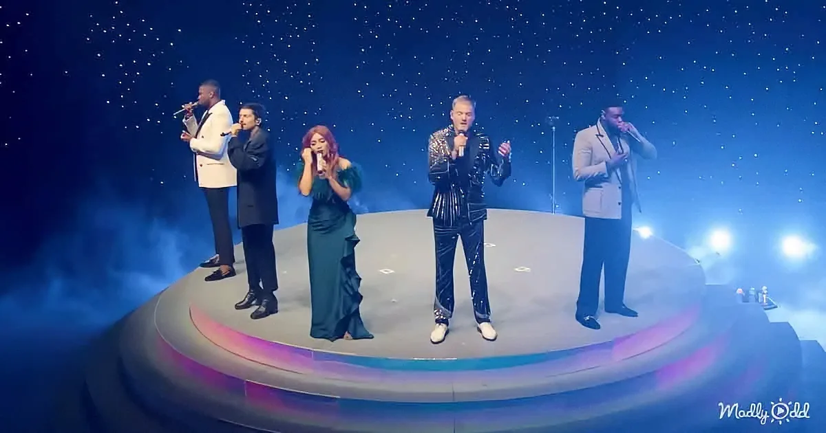 A group of five performers in formal attire sing on a stage with a starry backdrop.