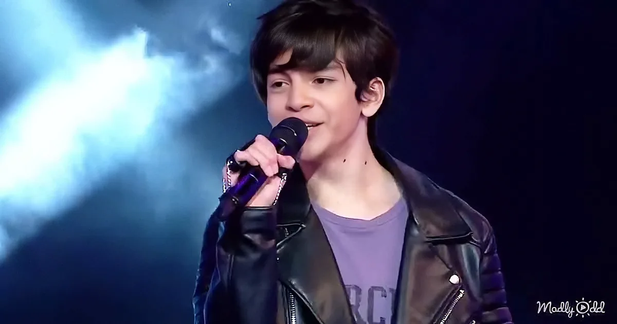 A person in a leather jacket holds a microphone, performing on stage with dramatic lighting.