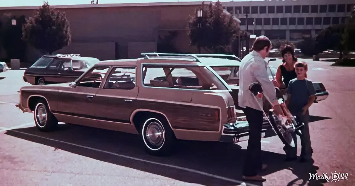 A vintage station wagon with wood paneling is parked in a lot, with a man and two children standing nearby.