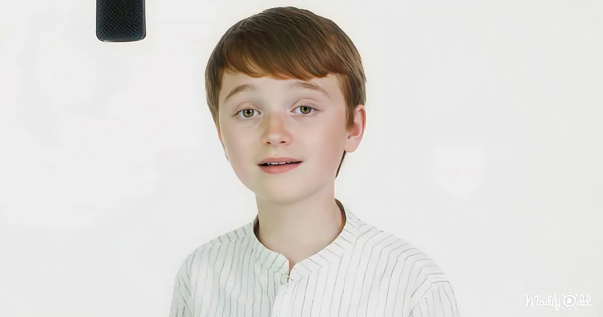 A young boy with short brown hair and green eyes, wearing a white striped shirt, stands against a plain white background.