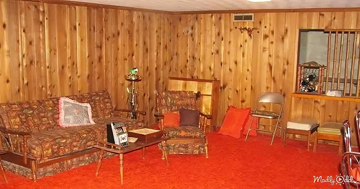 A vintage living room with wood-paneled walls, floral furniture, and a red carpet.