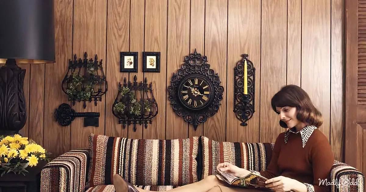 A woman in a brown sweater sits on a striped couch, holding a magazine, with a vintage wall clock and decor behind her.