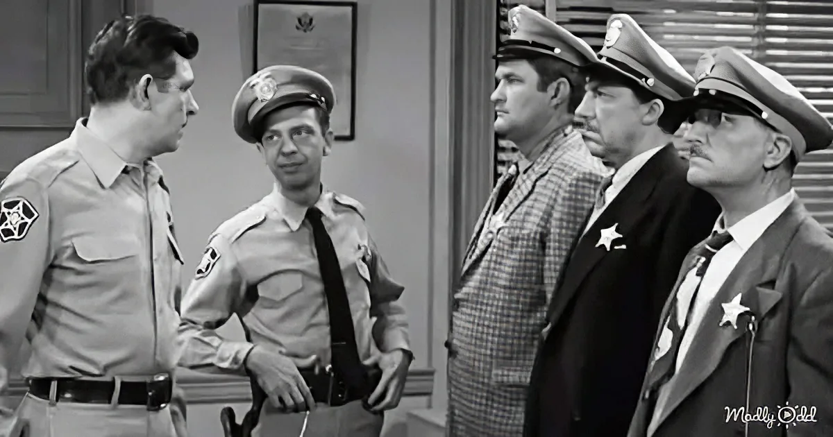 A man in a sheriff's uniform stands in a room, talking to another man in a similar uniform, while others in various...