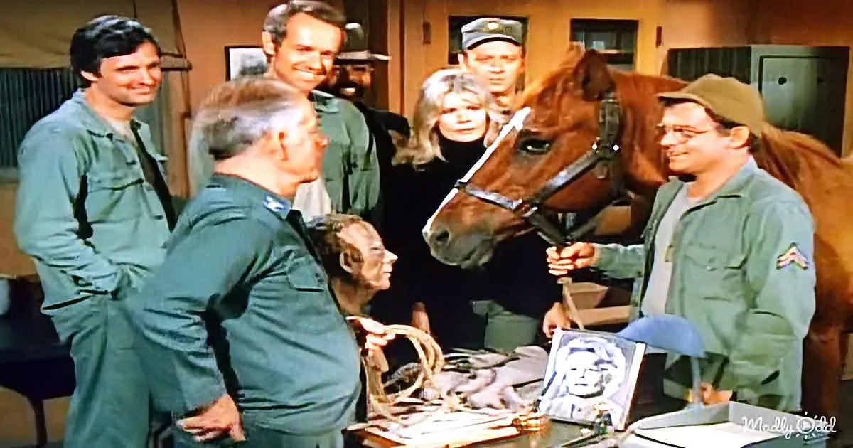 A man in green uniform holds a horse's bridle, surrounded by others in similar attire, with a portrait and rope on a table.