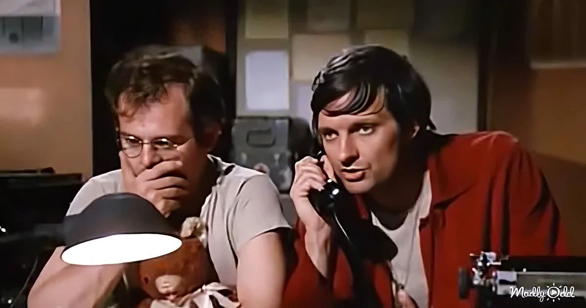 A man in a red jacket is on the phone, while another man in a white shirt holds a teddy bear and covers his mouth.