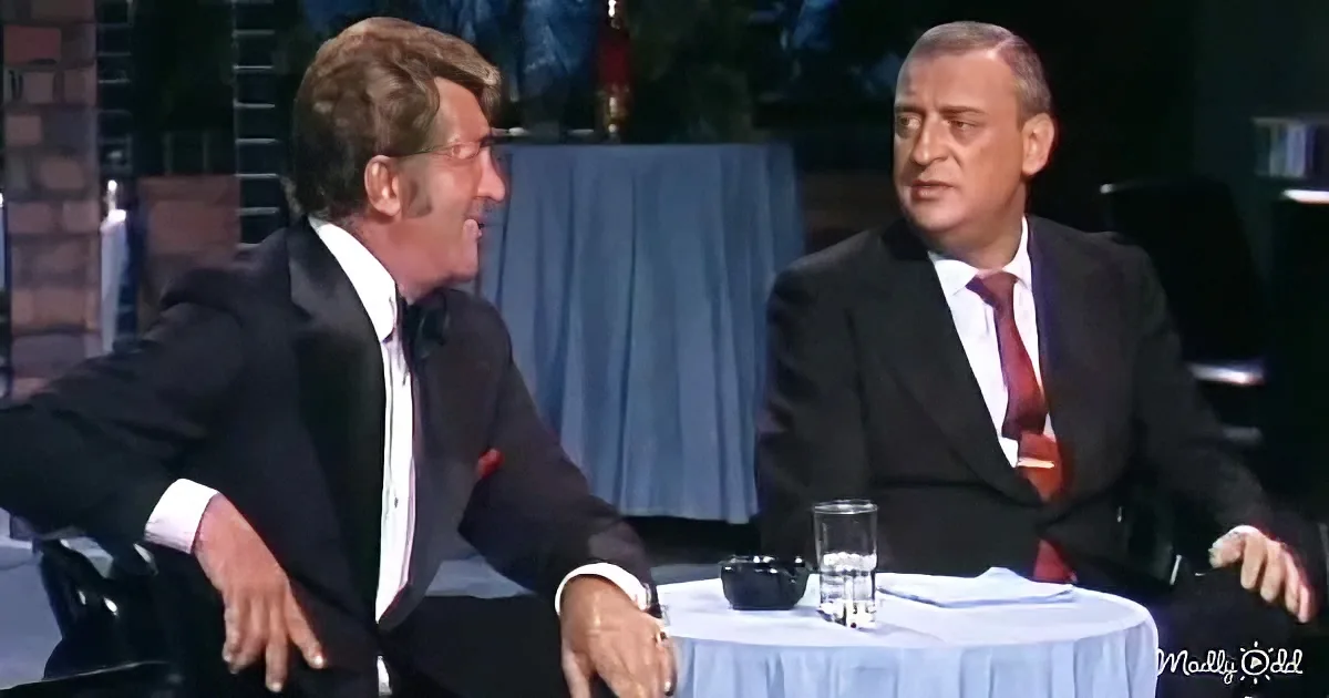 Two men in suits are seated at a table, one leaning forward, both appearing engaged in a discussion.