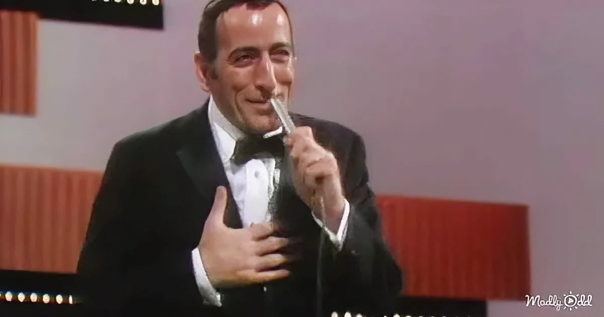 A man in a tuxedo is holding a microphone and giving a thumbs-up gesture.