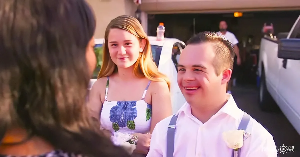 A man in a white shirt and suspenders smiles at a woman in a white dress with blue floral patterns.