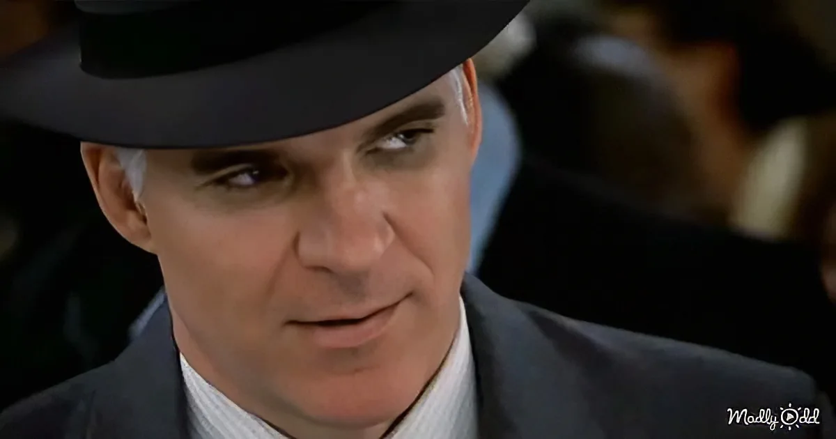 A man in a suit and hat, looking serious, with a blurred background.