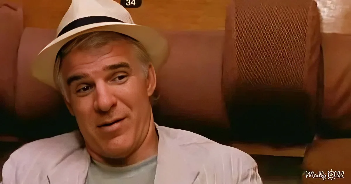 A man wearing a white hat and light-colored jacket sits in a theater seat, looking to the side.