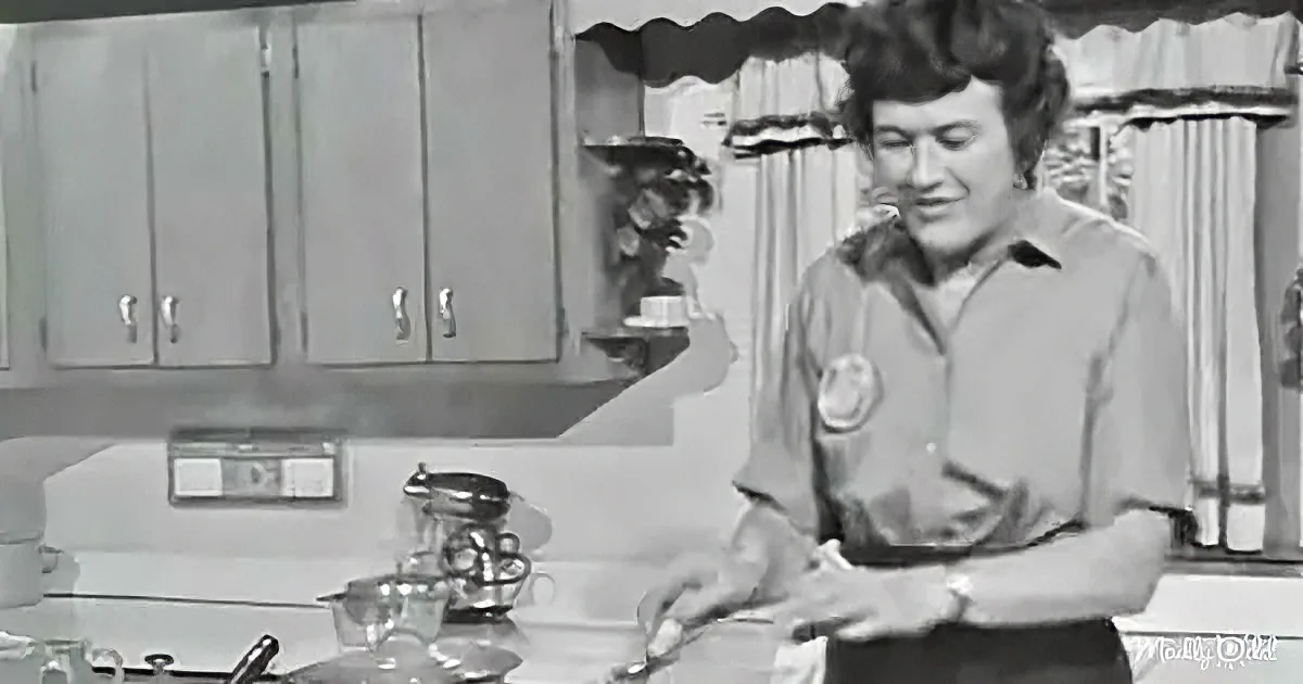 A person in a kitchen, wearing a shirt with a badge, is preparing food at a counter.