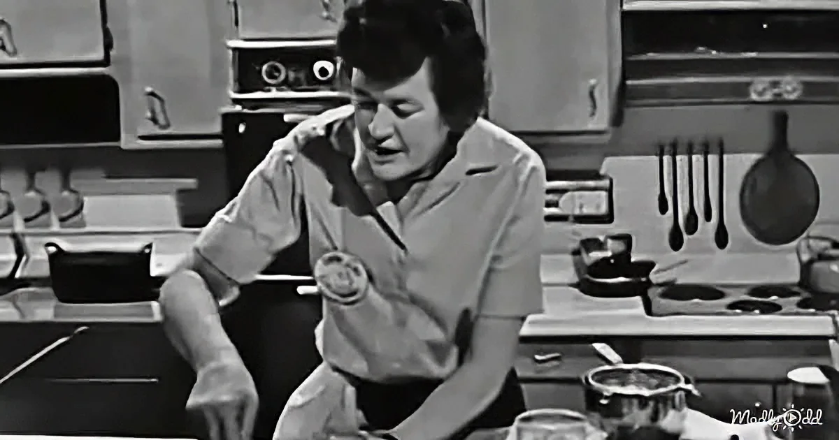 A woman in a kitchen, holding a spoon, appears to be in the middle of cooking or preparing food.