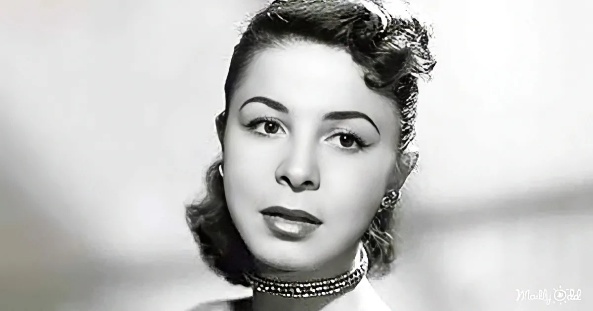 A woman with styled hair, wearing a pearl choker, and a black-and-white portrait.
