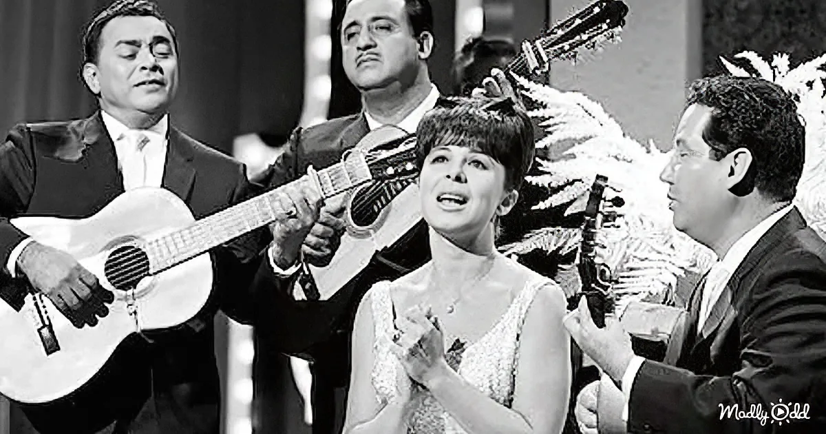 A woman in a white dress sings passionately, surrounded by musicians playing guitars.