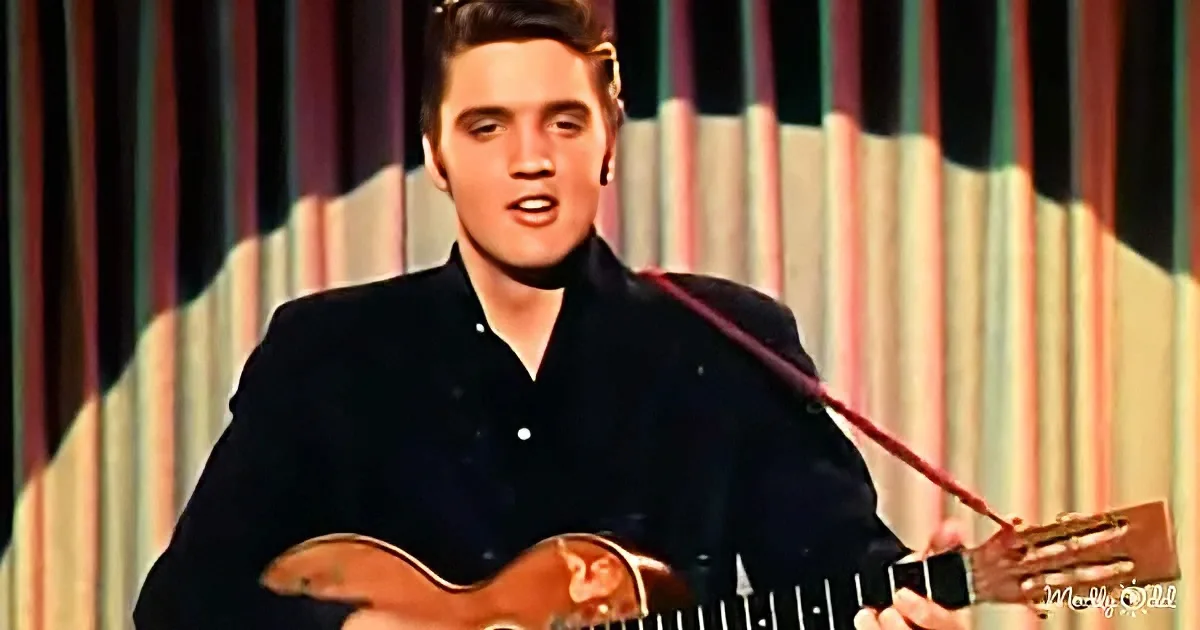 Elvis Presley in a black shirt singing while playing a guitar on stage.