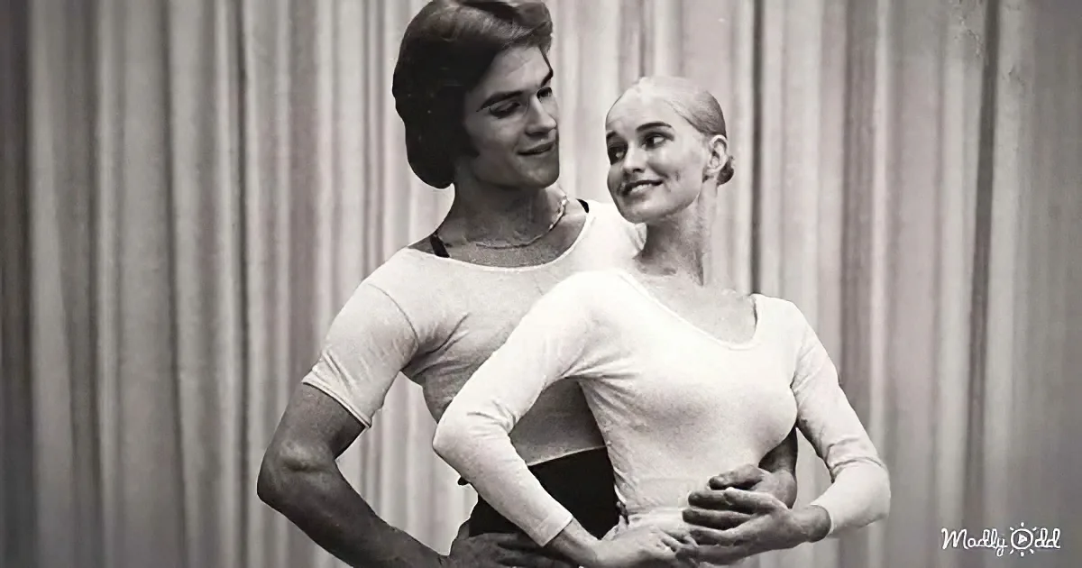 A ballet couple in white leotards stands together, the man holding the woman's waist.