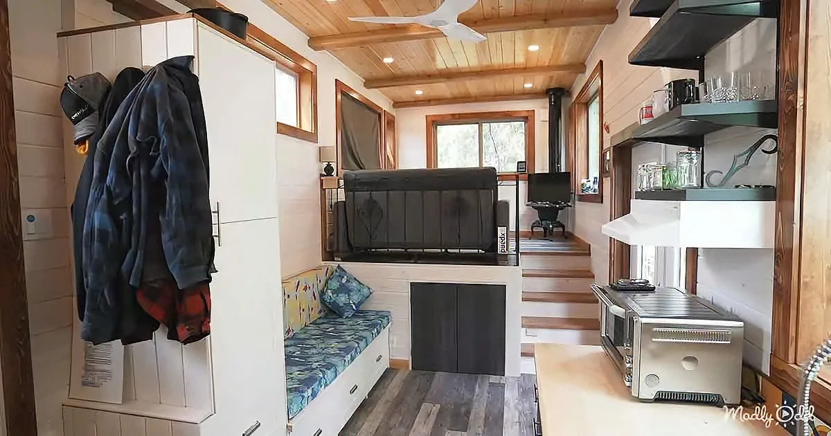 A cozy, compact tiny house interior with a bench, fireplace, shelves, and wooden accents.