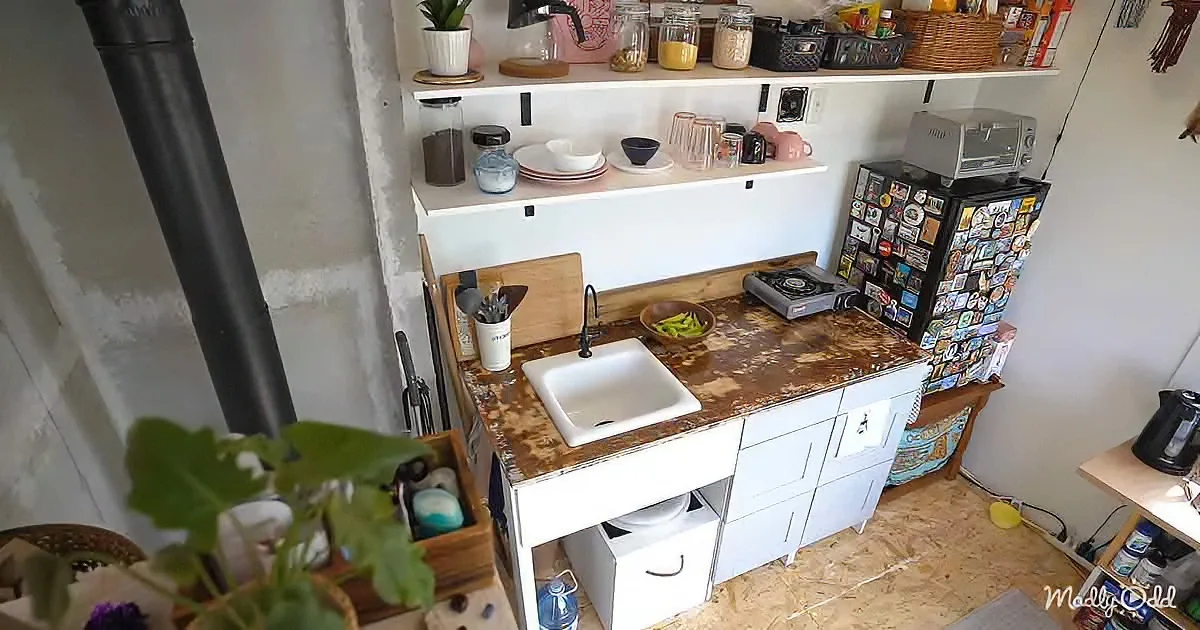 A compact kitchen with a rustic countertop, white cabinets, and a black refrigerator adorned with stickers.