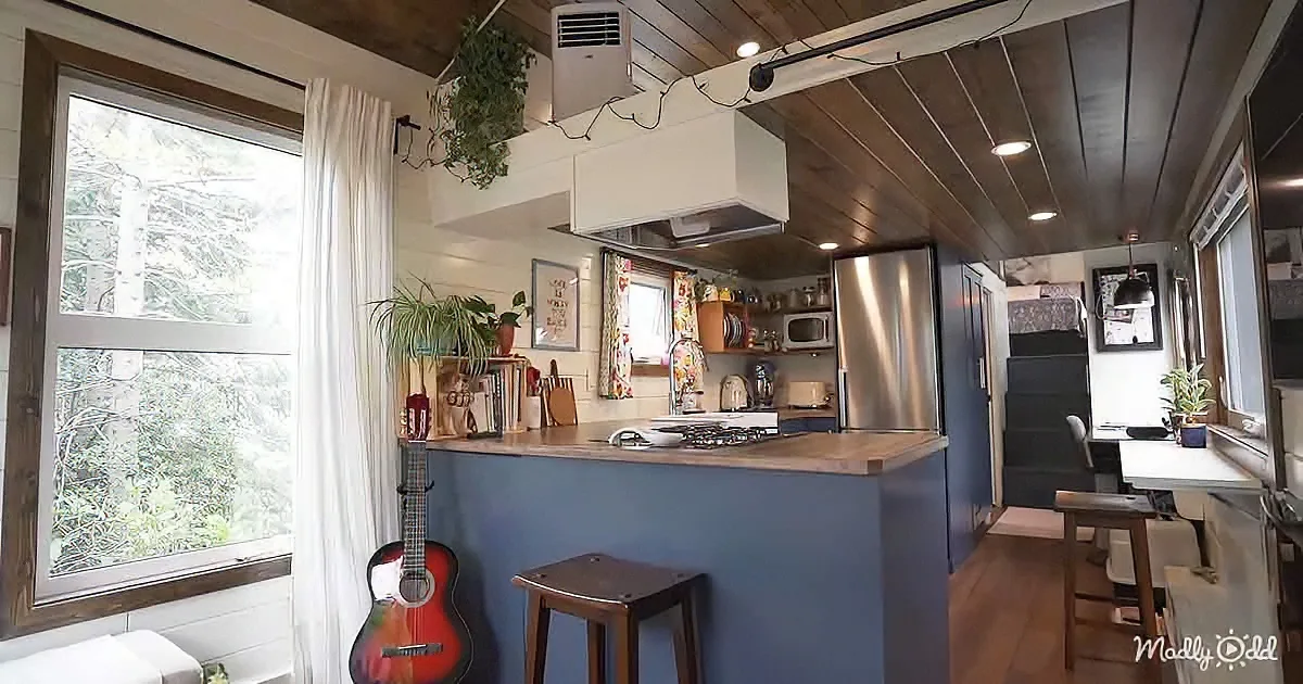 A cozy kitchen with a blue island, guitar, and wooden ceiling in a tiny home.