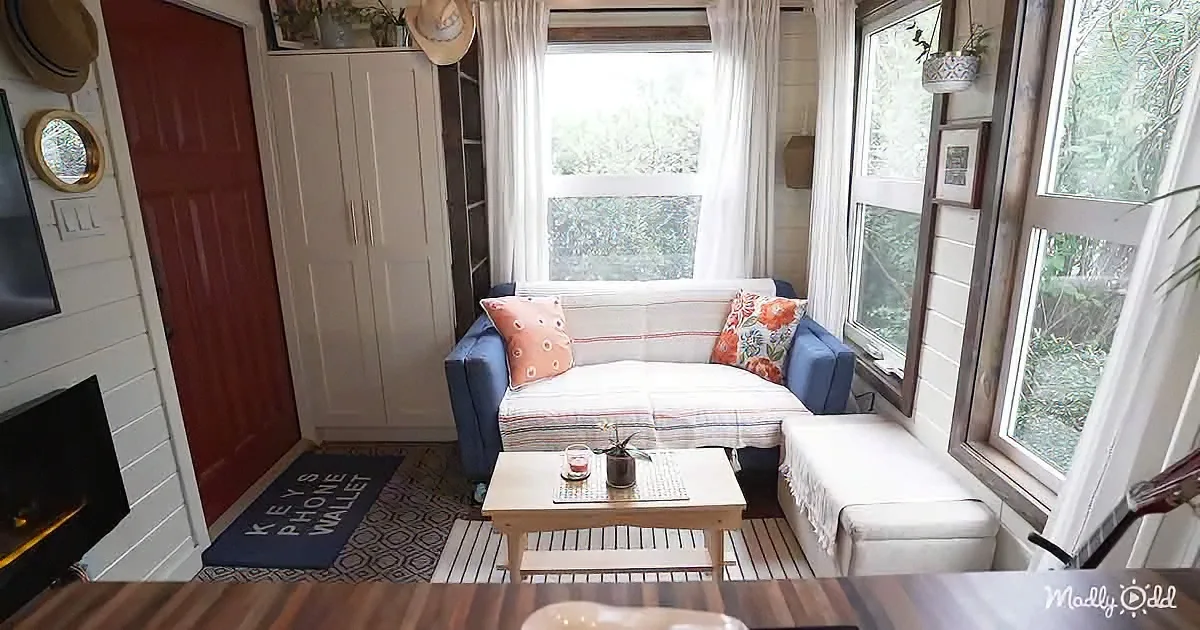 A cozy living room with a blue couch, white curtains, and a wooden coffee table.