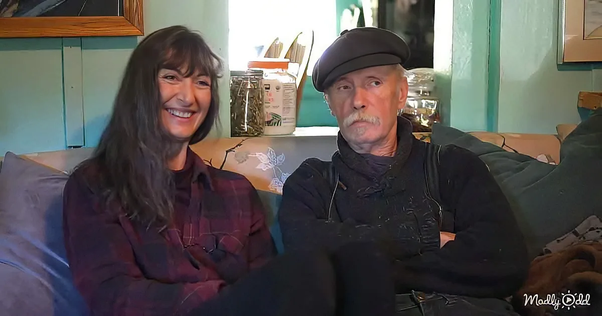 A woman in a plaid shirt smiles while sitting next to a man in a cap on a couch.