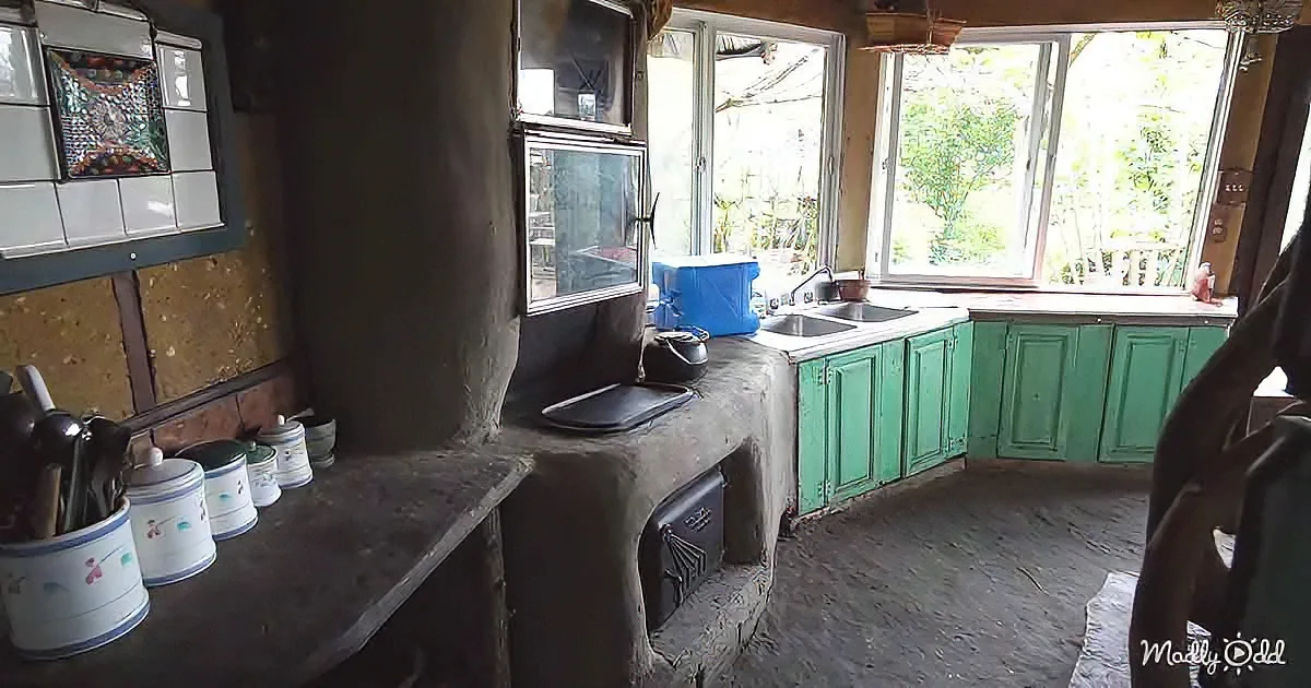 A rustic kitchen with green cabinets, a stone countertop, and a window view of trees.