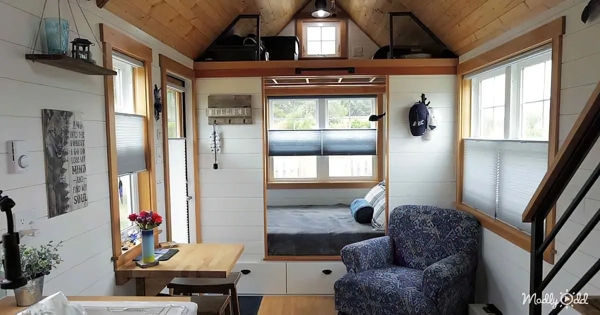 A cozy tiny house interior with a loft bed, wooden ceiling, and a small dining area.