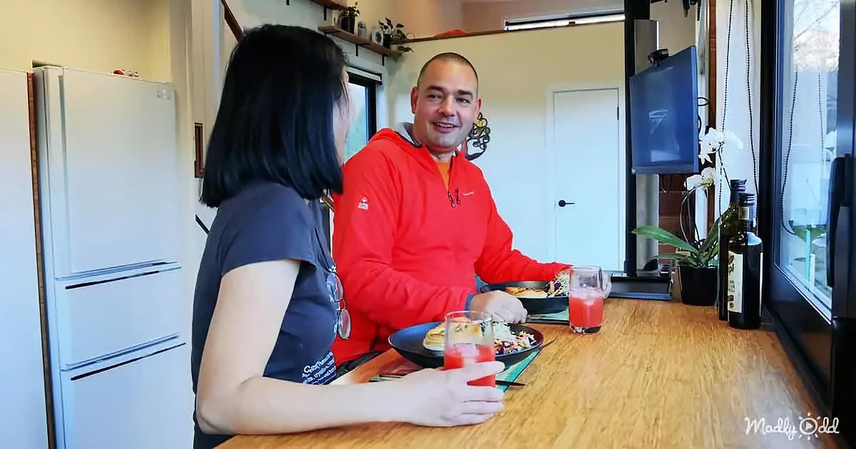 A man and woman sit at a kitchen counter, enjoying a meal together with drinks.