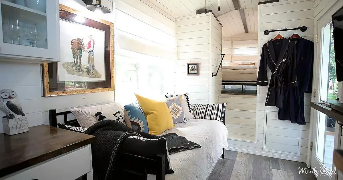 A cozy, well-decorated tiny house bedroom with a bed, colorful pillows, a robe, and a painting of a horse.