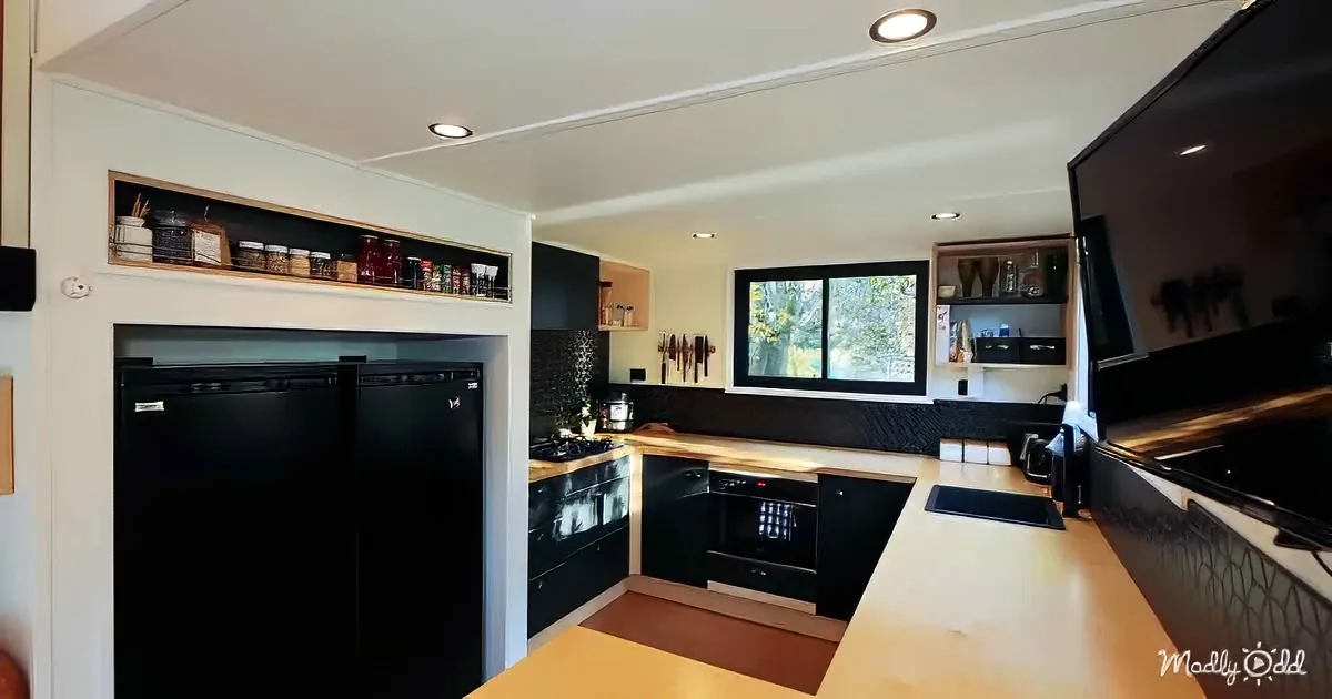 A modern kitchen with black appliances, wooden countertops, and a window showing greenery outside.