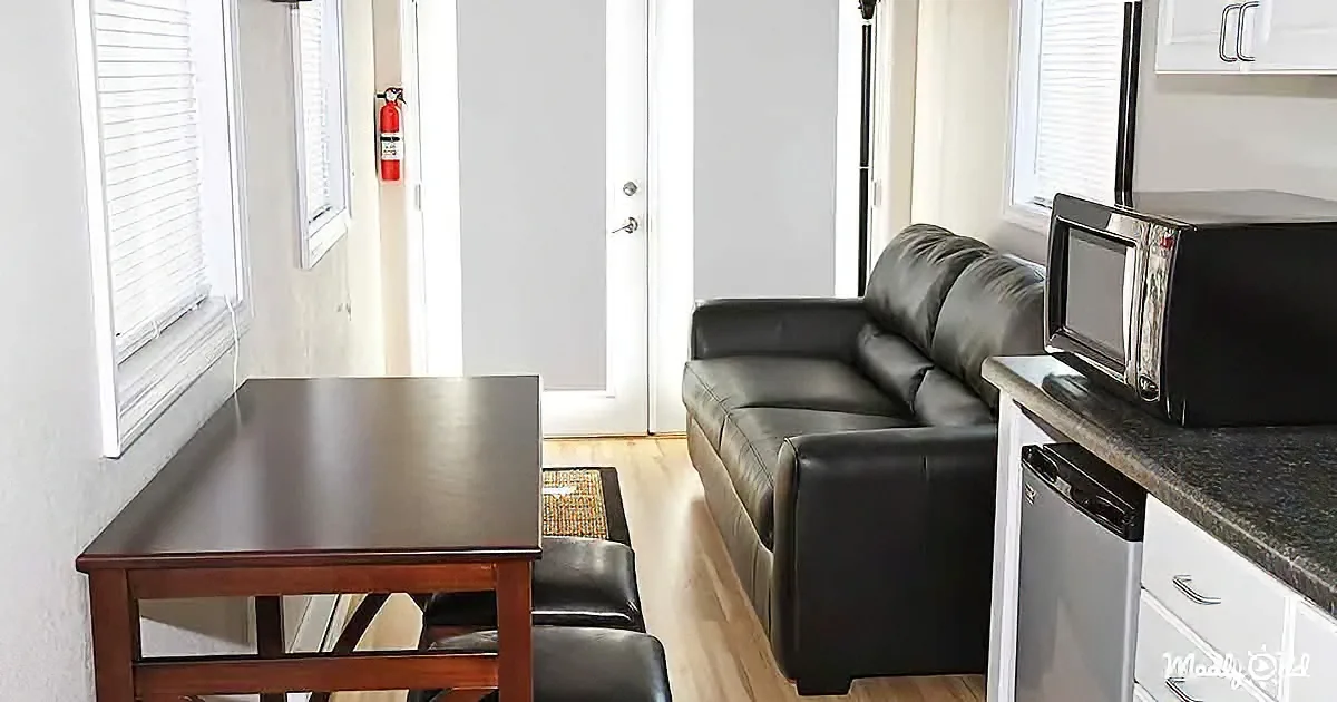 A black leather couch sits beside a kitchen counter with a microwave and small table nearby.