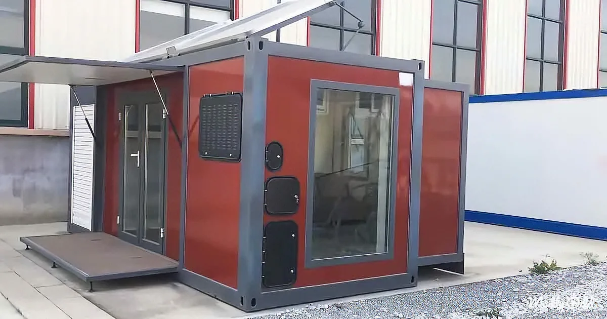 A red and gray modular structure with a glass door and side panels, set against a building with red and white walls.