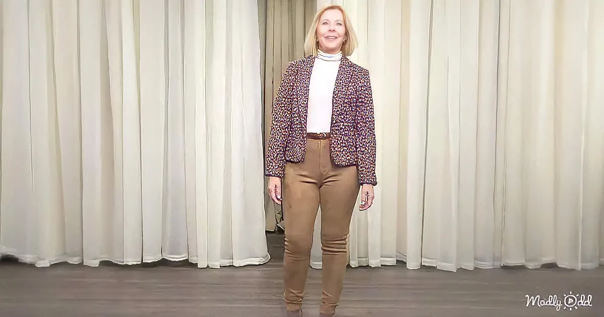 A woman in a leopard print blazer and beige pants stands in front of a white curtain.