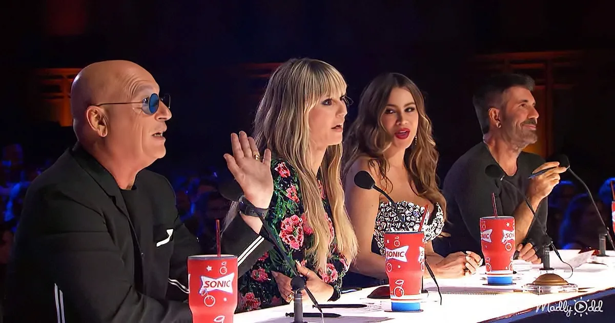 Four judges sit at a table with microphones, Sonic drinks, and a dark audience in the background.