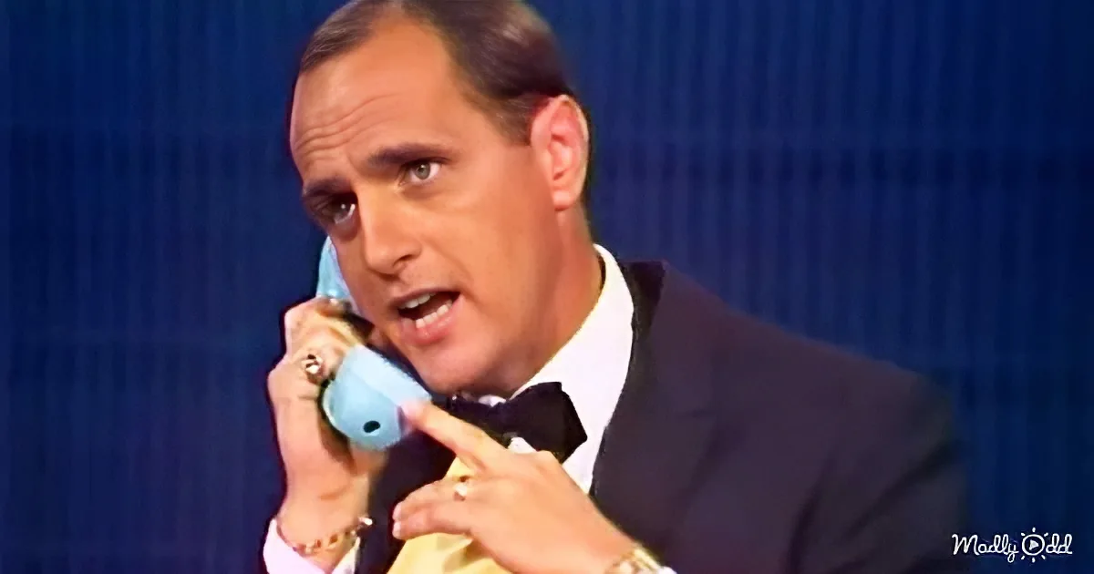 A man in a suit and bow tie is holding a blue telephone to his ear, appearing to be engaged in a conversation.