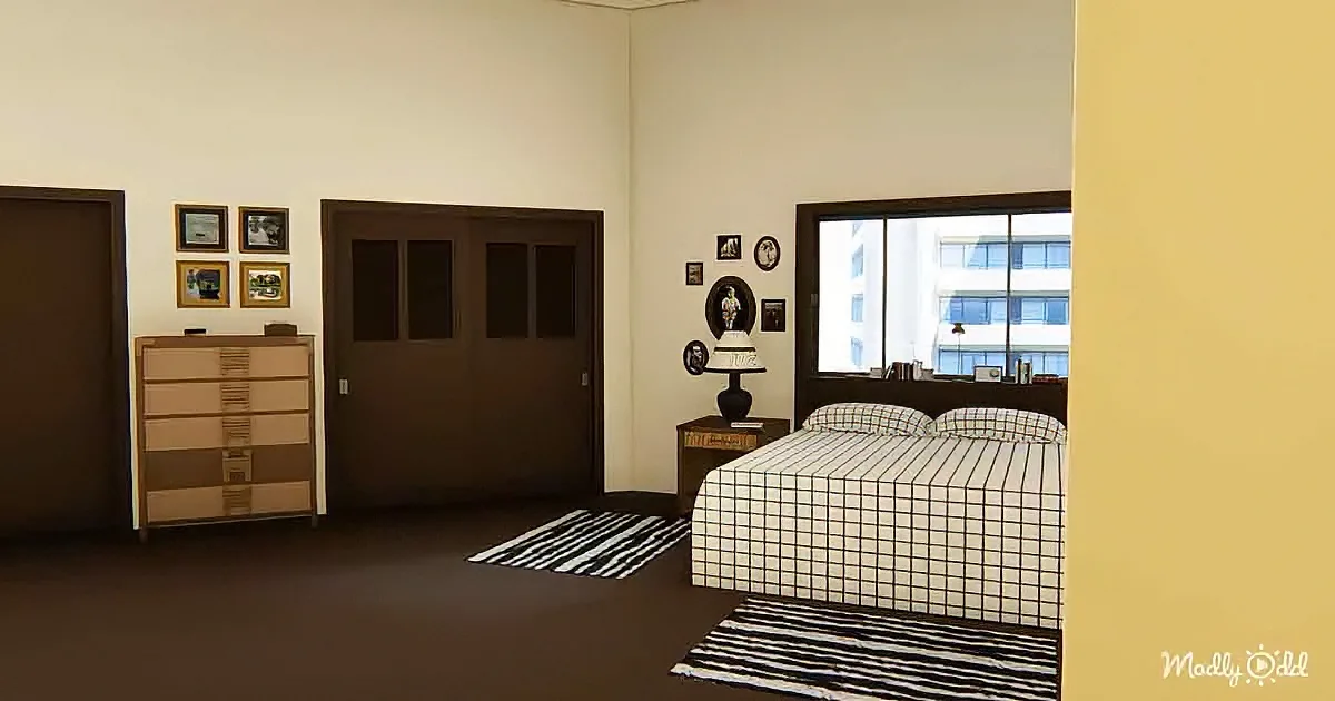 A cozy bedroom with a bed, dresser, framed pictures, and a window showing a building outside.