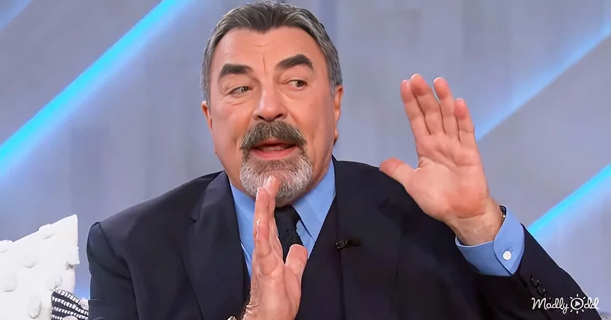 A man in a suit gestures with his hands while speaking, wearing a blue shirt and tie.