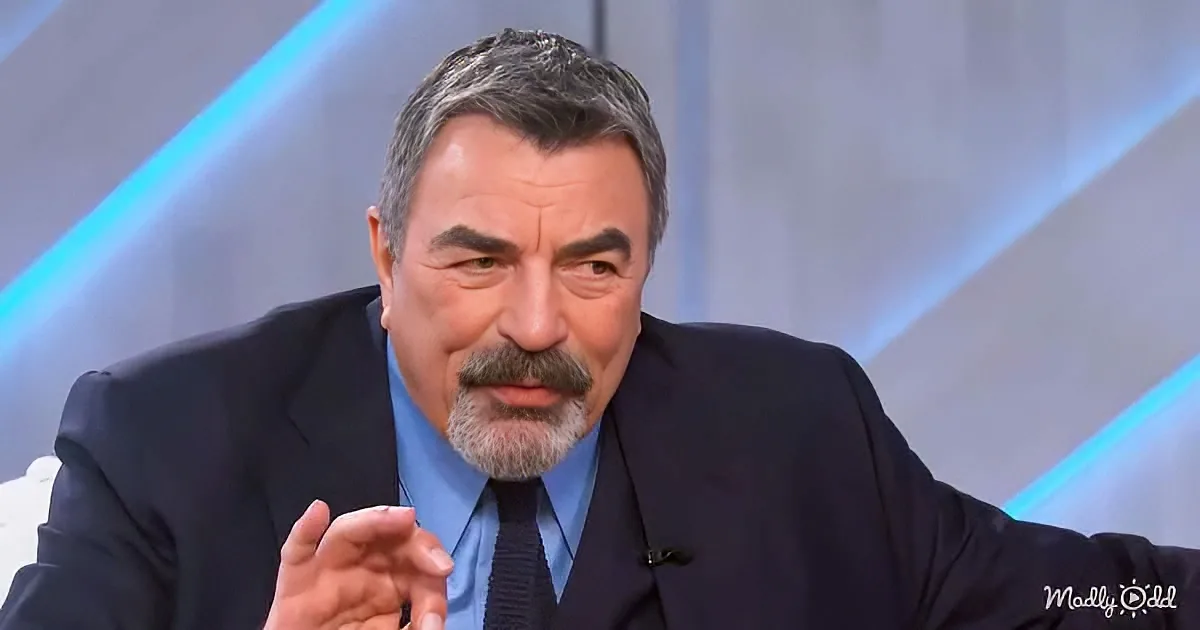 A man in a suit and tie is gesturing with his right hand while speaking.
