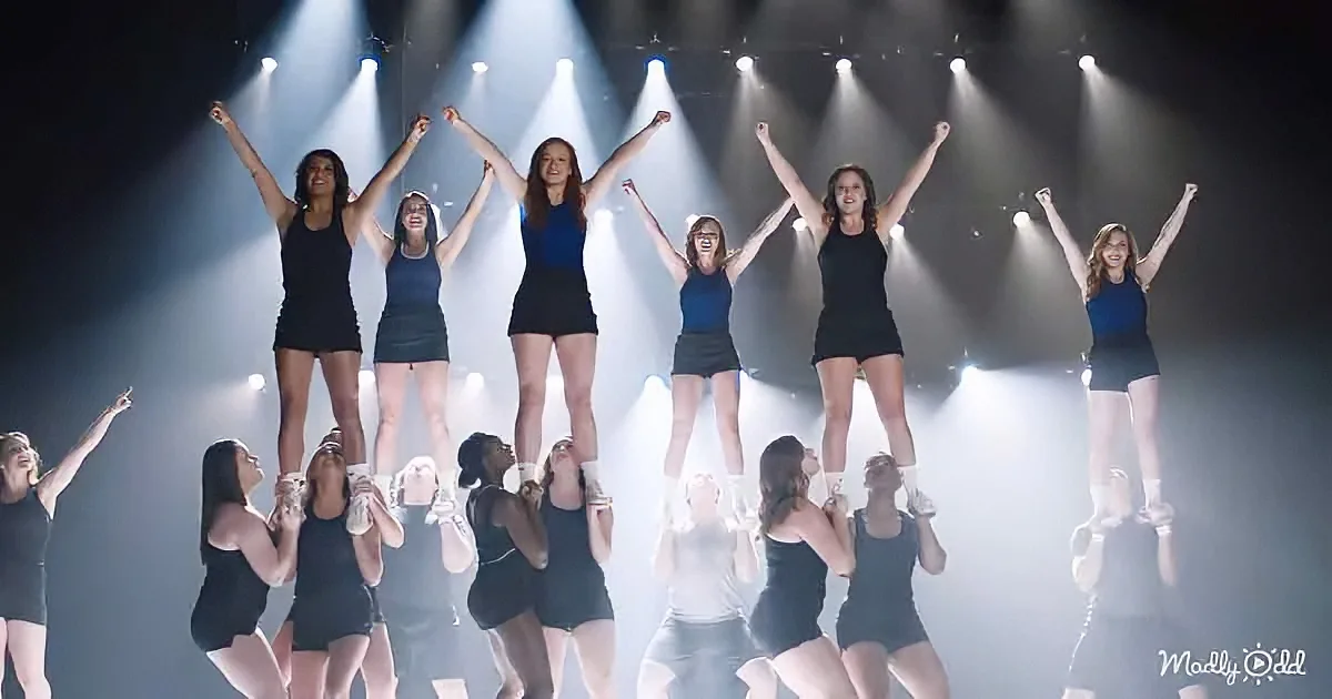 A group of cheerleaders perform a pyramid formation on stage under bright lights.