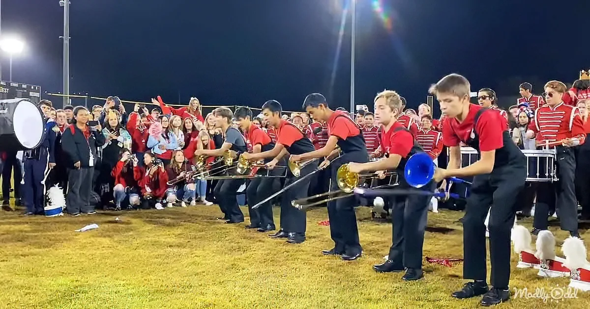 A marching band performs on a field at night, with students in red shirts and black pants playing brass instruments.