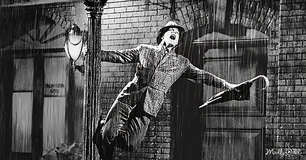 A man in a plaid suit and hat dances joyfully in the rain, holding an umbrella.