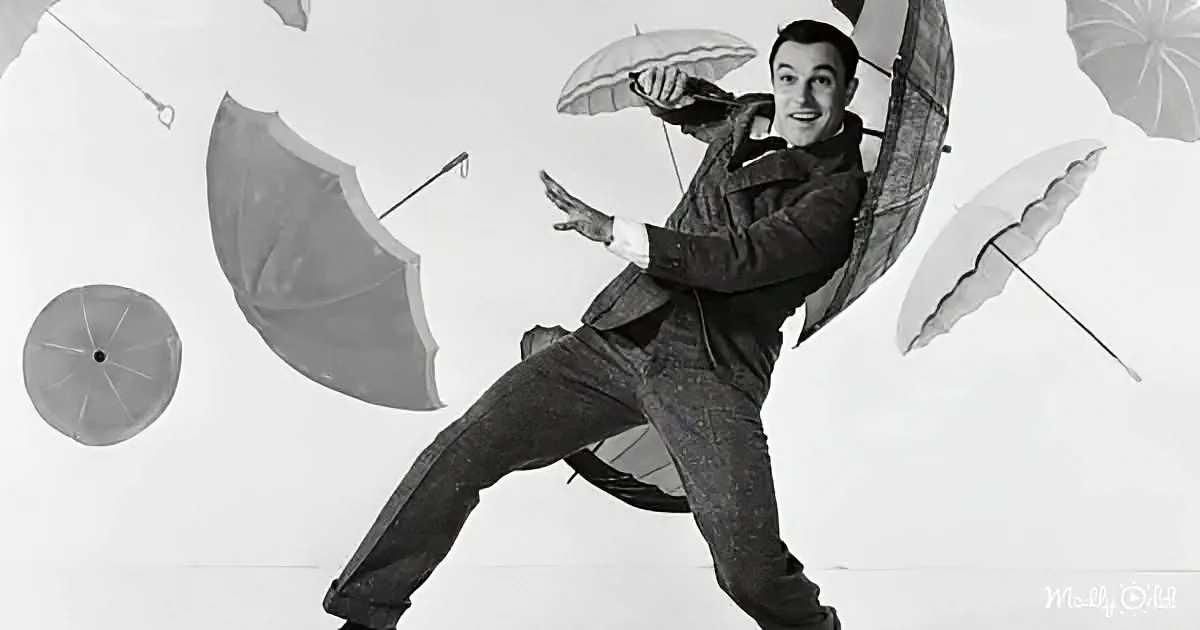 A man in a suit dances joyfully with umbrellas floating around him.