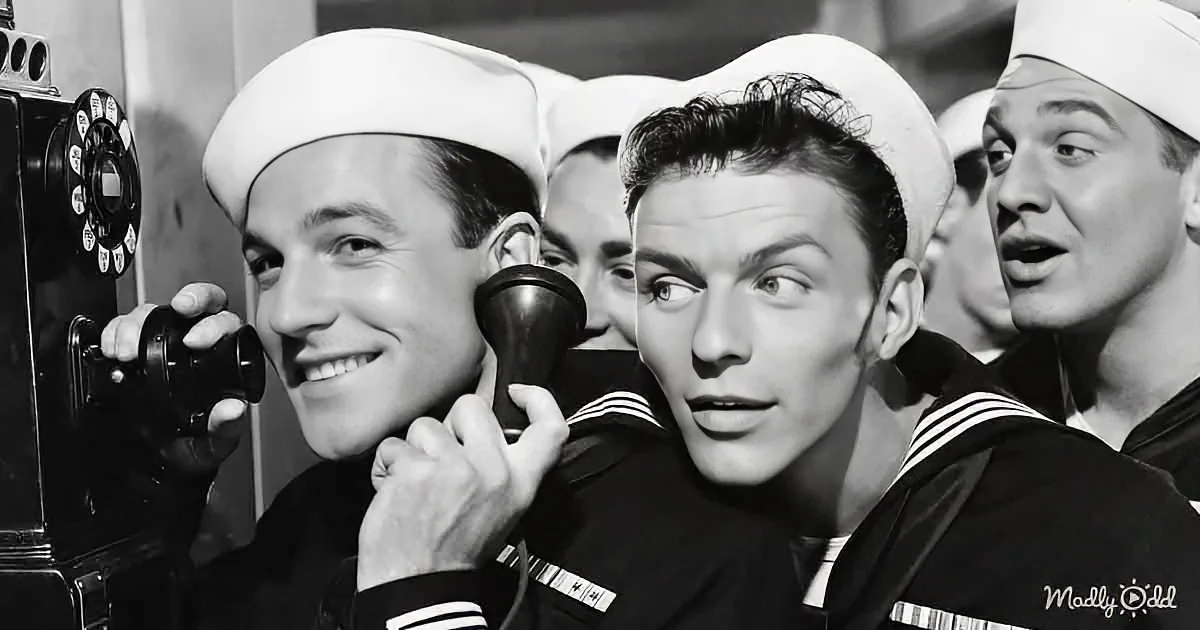 A sailor in a sailor suit holds a camera, smiling, with others in similar attire in the background.